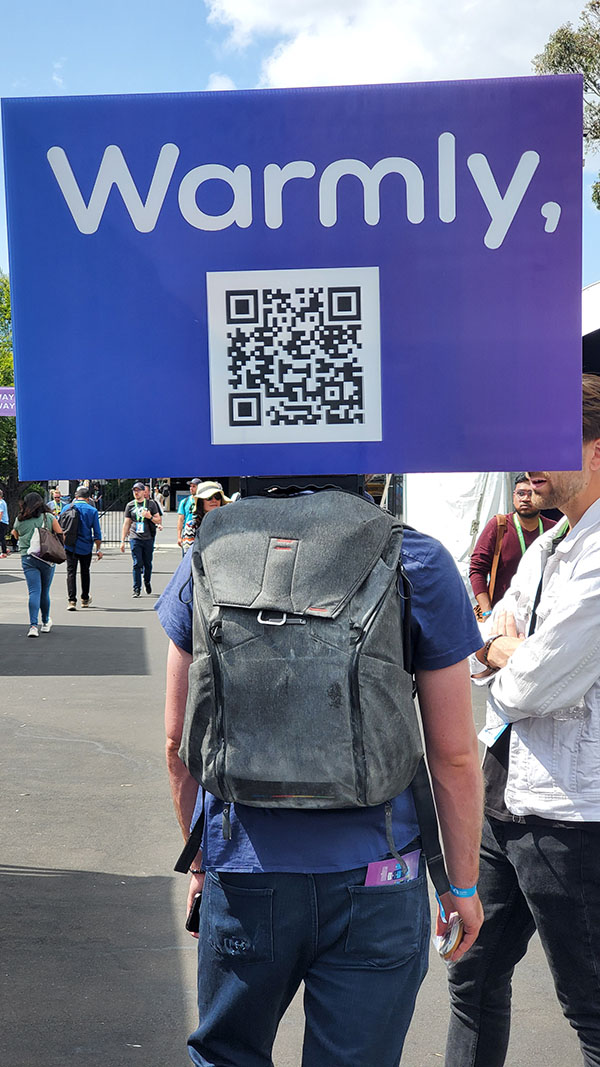 SaaStr attendee with purple cardboard sign on back that says Warmly with QR code