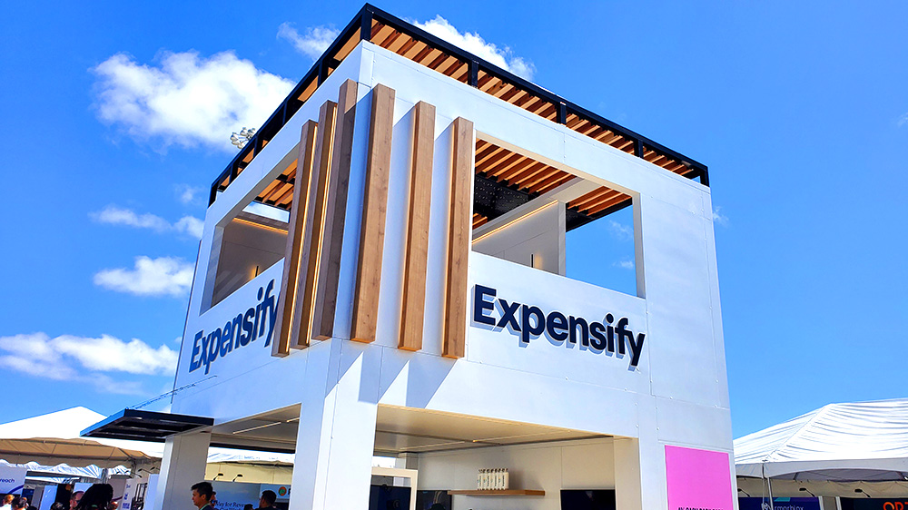 Large white Expensify booth at SaaStr 2022 with blue sky and clouds in background