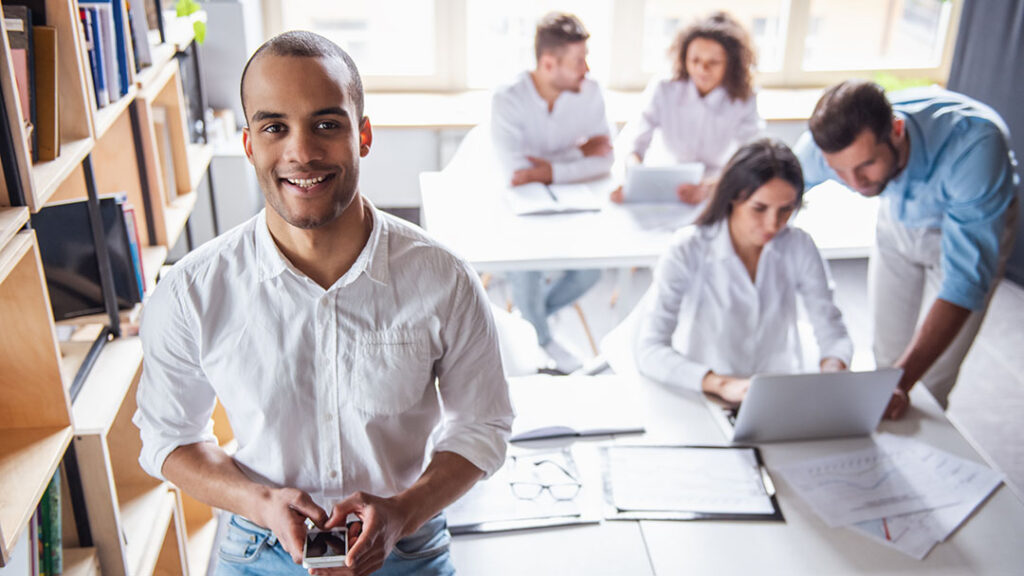 young entrepreneur in brightly lit office setting with employees working collaboratively in background