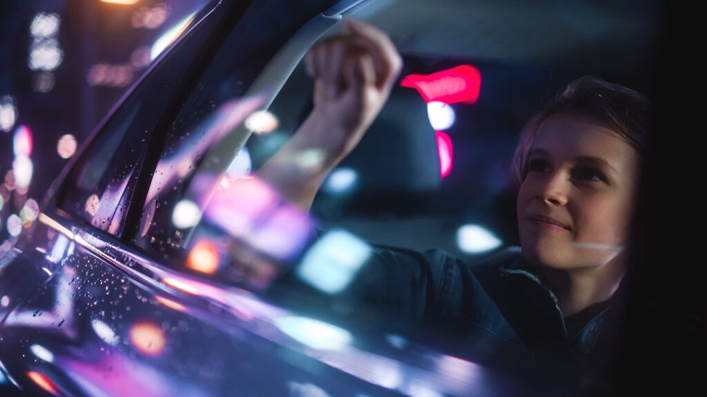 Woman smiling and looking out the window of car with neon lights reflecting off the glass