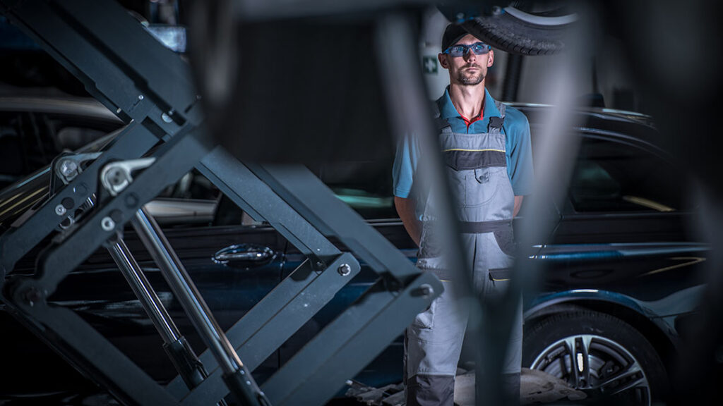 View of an automotive technician tradesman in the background with unrecognizable close up view engine components in the foreground