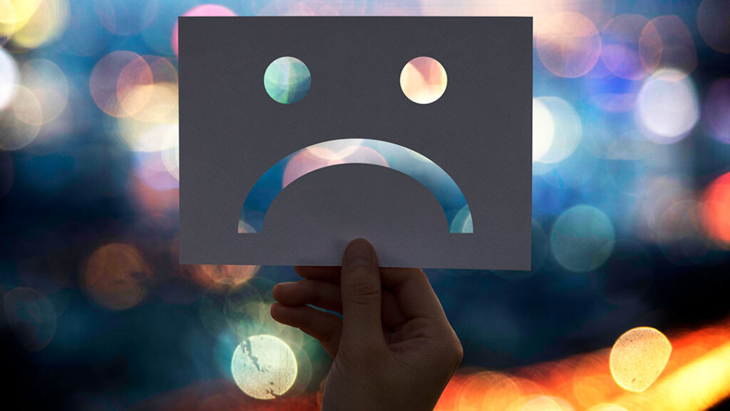 a hand holding an index card with a frown face cut out of it representing a bad customer experience